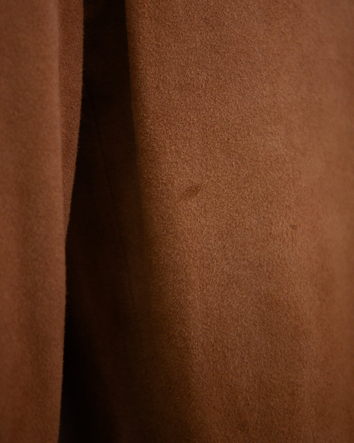 A close-up of a brown suede or suede-like fabric surface with a vertical seam and a few small dark specks.