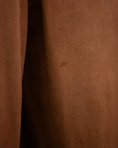 A close-up of a brown suede or suede-like fabric surface with a vertical seam and a few small dark specks.