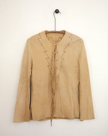 A light beige long-sleeve blouse with decorative tie-front laces and dark blue jeans, standing against a plain light gray wall on a hanger.