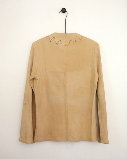 A tan suede long-sleeve top hanging on a black hanger against a plain off-white wall. The back of the garment features a central seam and a jagged, zig-zag stitched detail along the upper neckline.