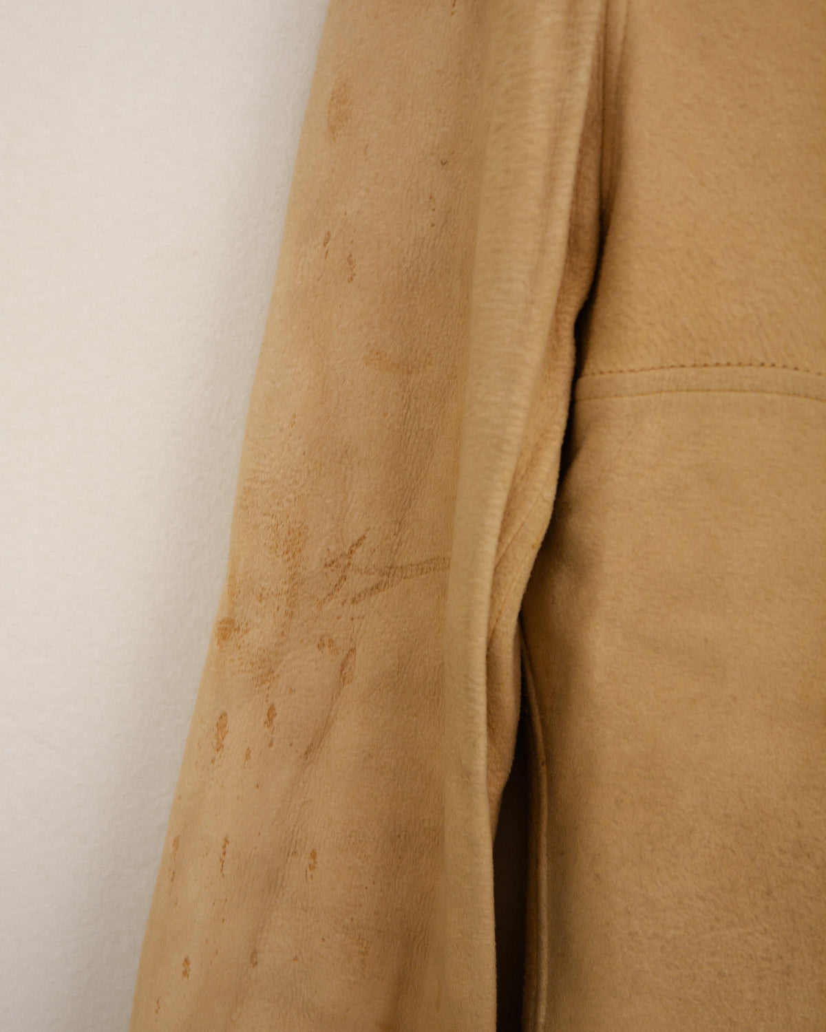 A close-up of a tan suede or leather fabric panel with visible stains and a stitched hem, shown against a plain off-white background.