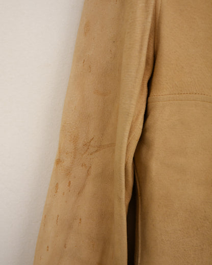 A close-up of a tan suede or leather fabric panel with visible stains and a stitched hem, shown against a plain off-white background.