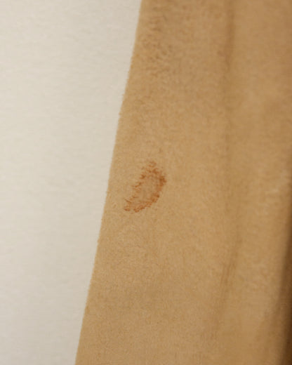 A close-up of a tan suede or leather fabric panel with visible stains and a stitched hem, shown against a plain off-white background.
