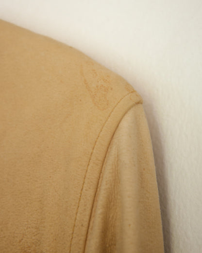 A close-up of a tan suede or leather fabric panel with visible stains and a stitched hem, shown against a plain off-white background.