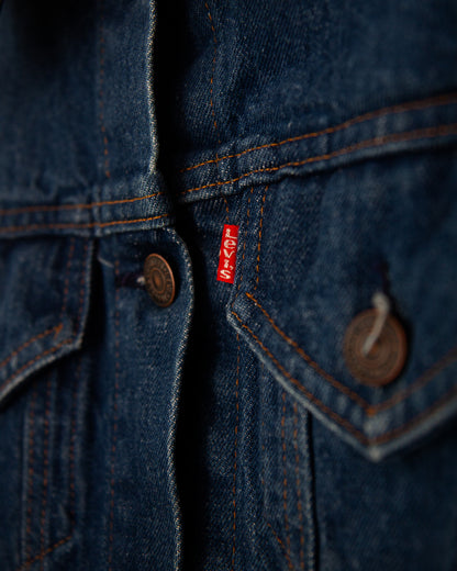 Close-up of a dark blue denim jacket showing the chest area with two buttoned flap pockets, dark metal buttons, and a small red Levi's tag on the right side.