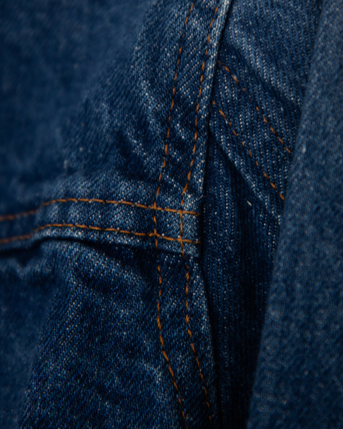 Close-up of a dark blue denim jacket showing the side seams and stiching.