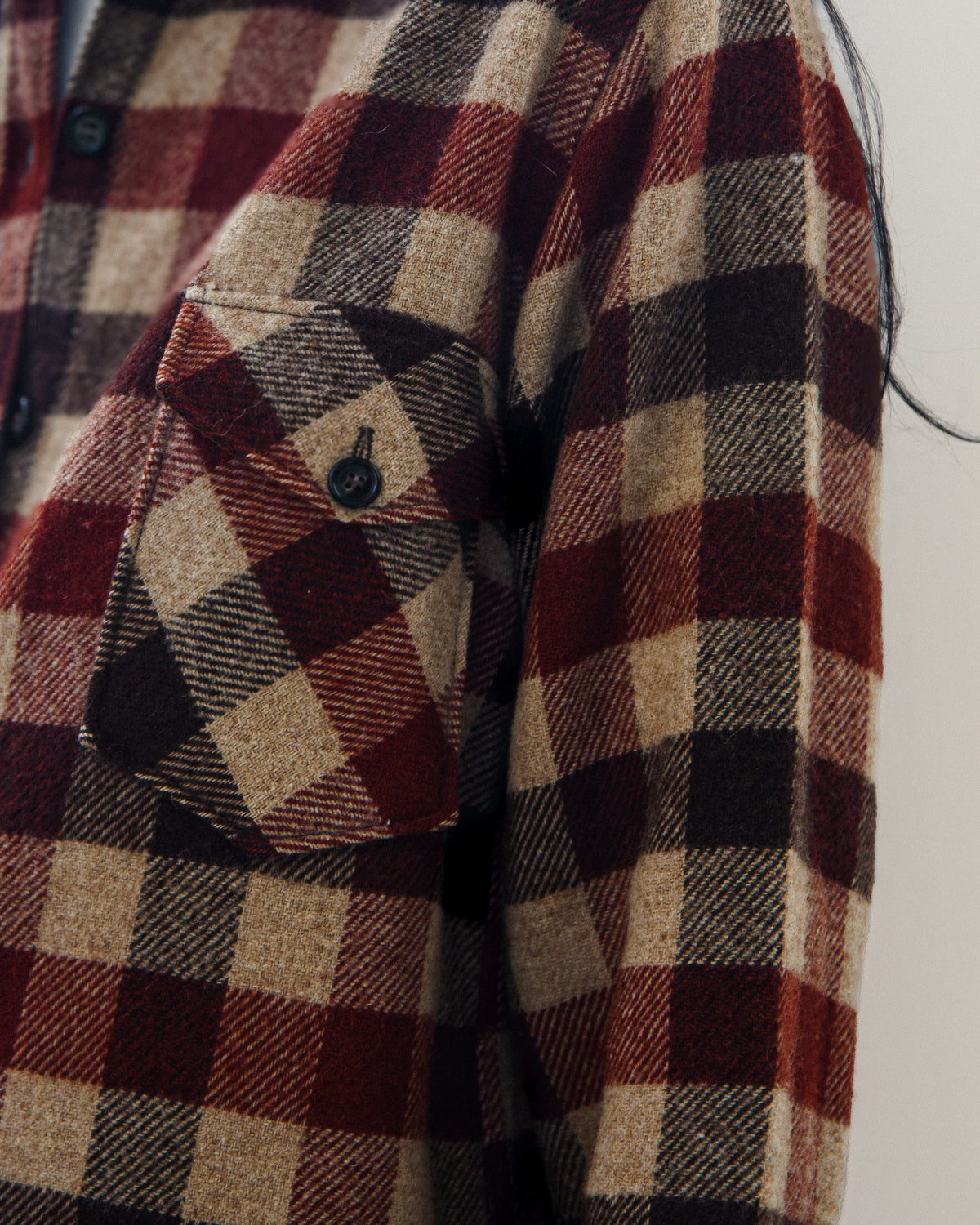 Close-up of a red, beige, and black plaid flannel shirt jacket with a chest pocket and button closure.