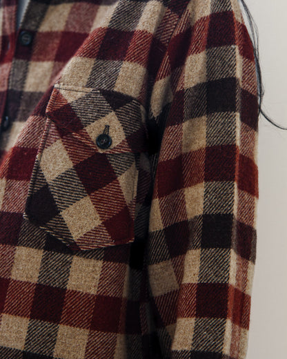 Close-up of a red, beige, and black plaid flannel shirt jacket with a chest pocket and button closure.