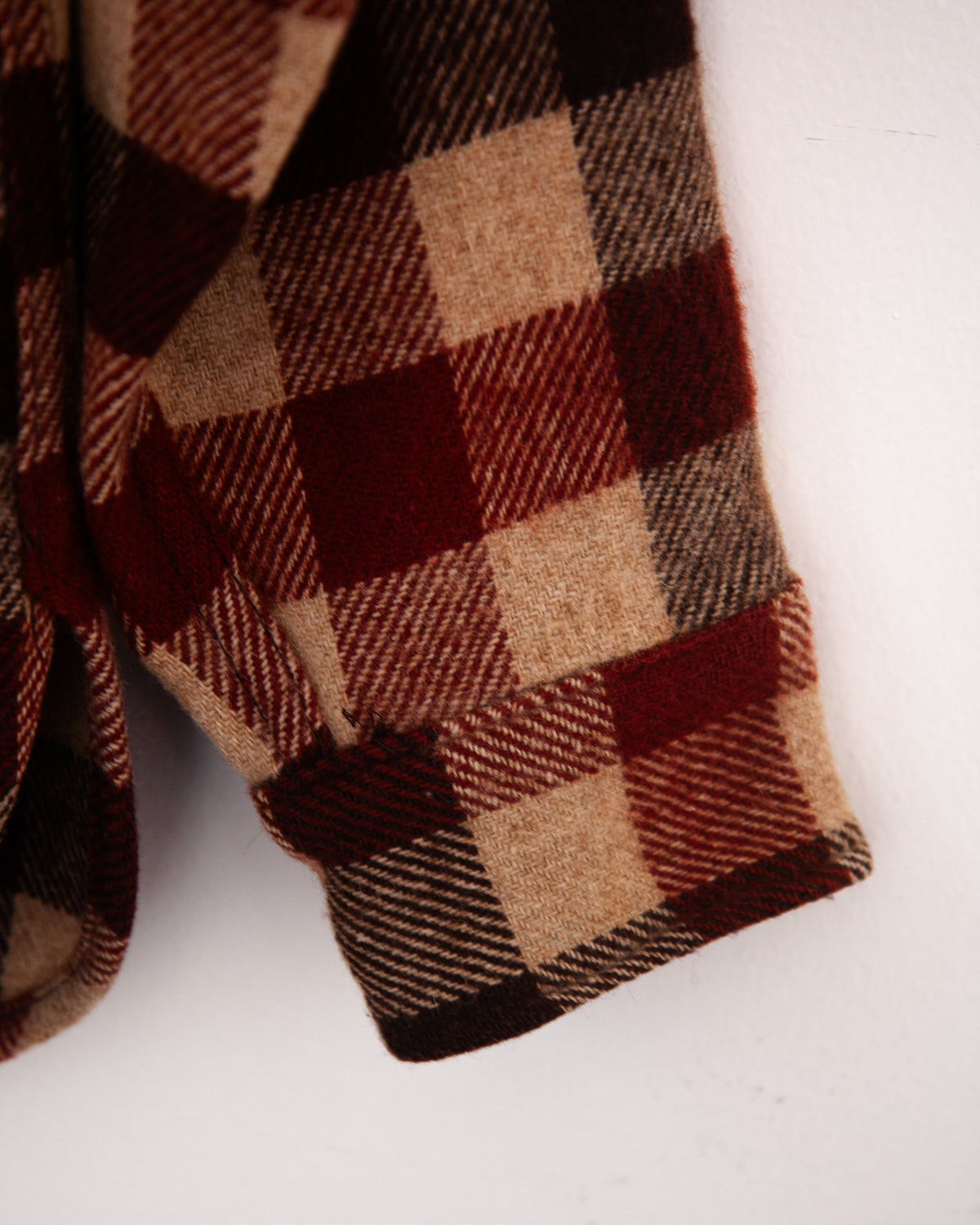 A close-up of a plaid wool or flannel fabric sleeve, showing a checkered pattern in dark red, tan, brown, and black on a plain white background.