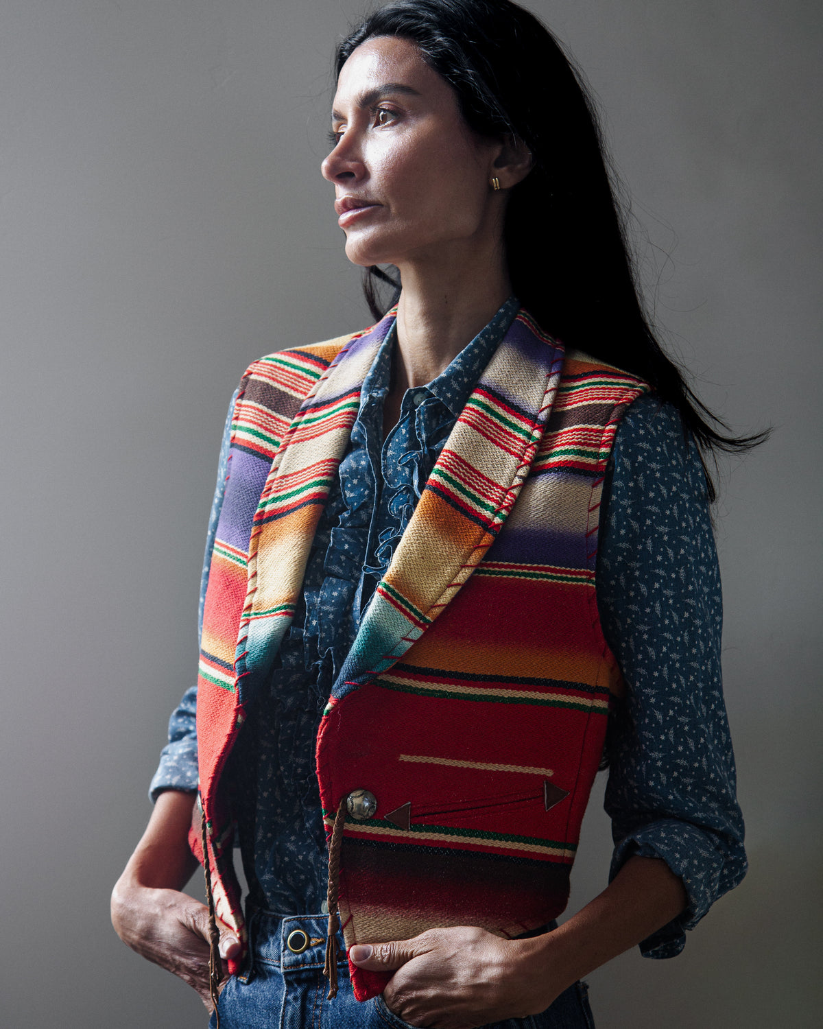 A sleeveless woven vest with a colorful serape-style striped pattern on a woman with a white background.