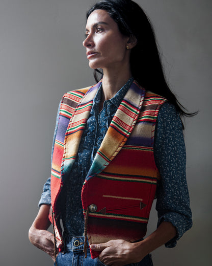 A sleeveless woven vest with a colorful serape-style striped pattern on a woman with a white background.
