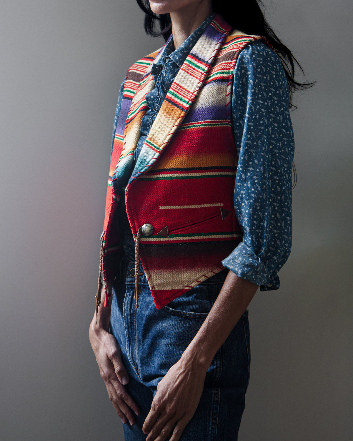 A sleeveless woven vest with a colorful serape-style striped pattern on a woman with a white background.