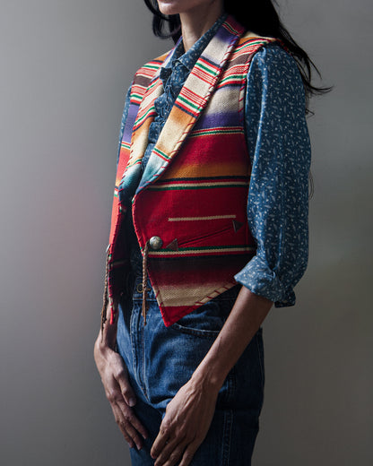 A sleeveless woven vest with a colorful serape-style striped pattern on a woman with a white background.