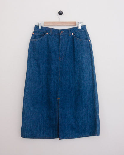 A blue denim midi skirt with a front slit, hanging on a wooden hanger against a plain white wall.