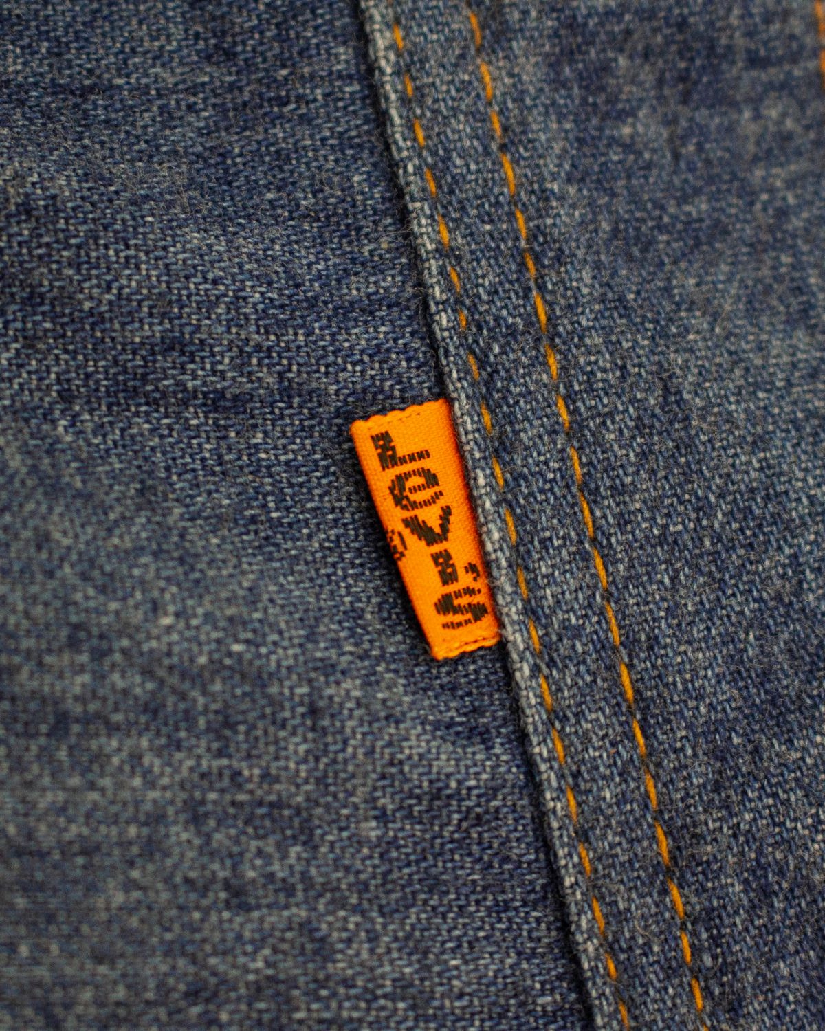 Close-up of a blue denim garment with orange contrast stitching and a small orange brand tab reading Levi's.