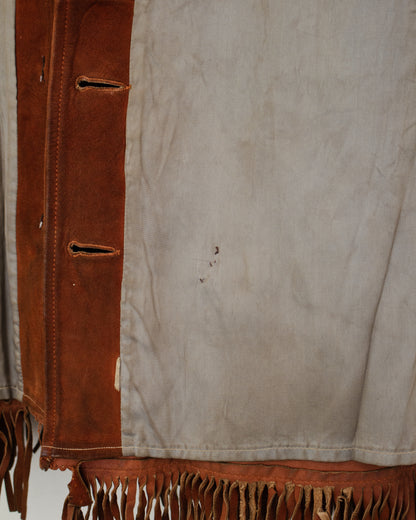 Close-up of a fringed garment or textile with a light beige suede-like body and a vertical brown suede panel with stitched openings and fringe. along the bottom.