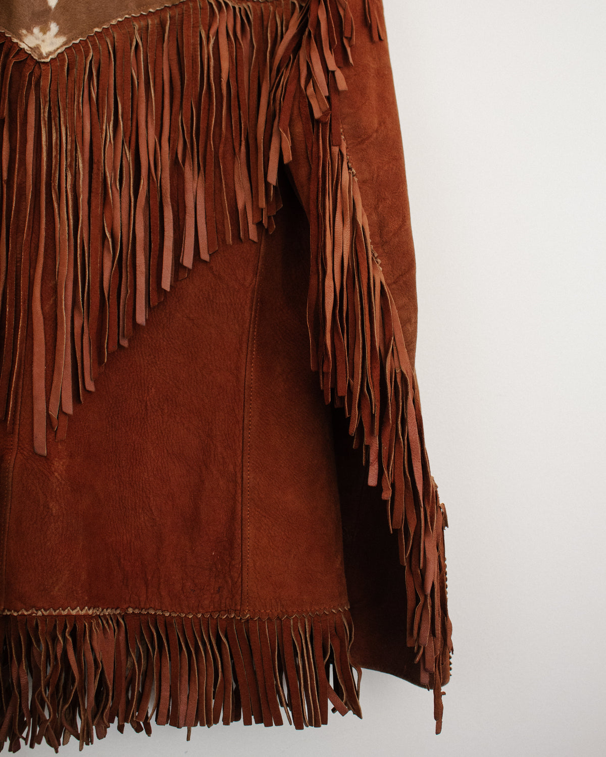 Close-up of a brown suede fringe garment, showing the texture of the suede and the layered fringe details against a plain white background.