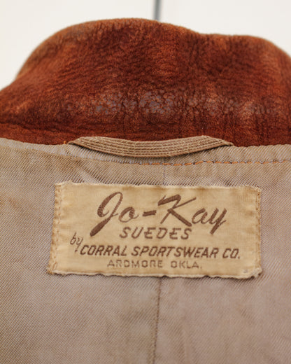 Close-up of the interior neck label of a vintage jacket, showing a beige fabric patch with brown text that reads 'Jo-Kay SUEDES by CORRAL SPORTSWEAR CO. ARDMORE OKLA.
