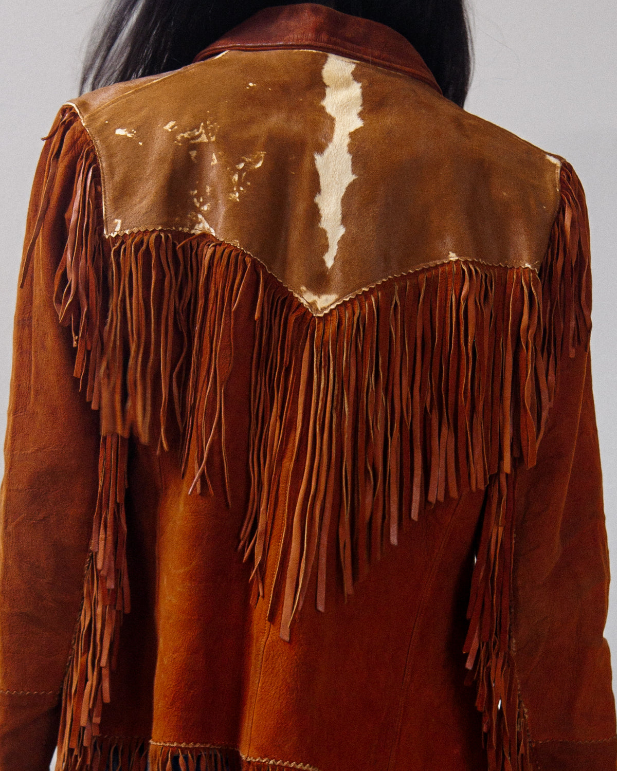 Close-up back view of a brown suede and leather fringe jacket.