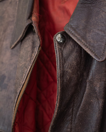 Close-up of a dark brown distressed leather jacket with a red quilted lining, showing the collar, zipper, and button detail.