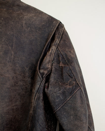 Close-up of a dark brown distressed leather jacket showing the shoulder seam, textured surface, and stitching details against a plain light background.