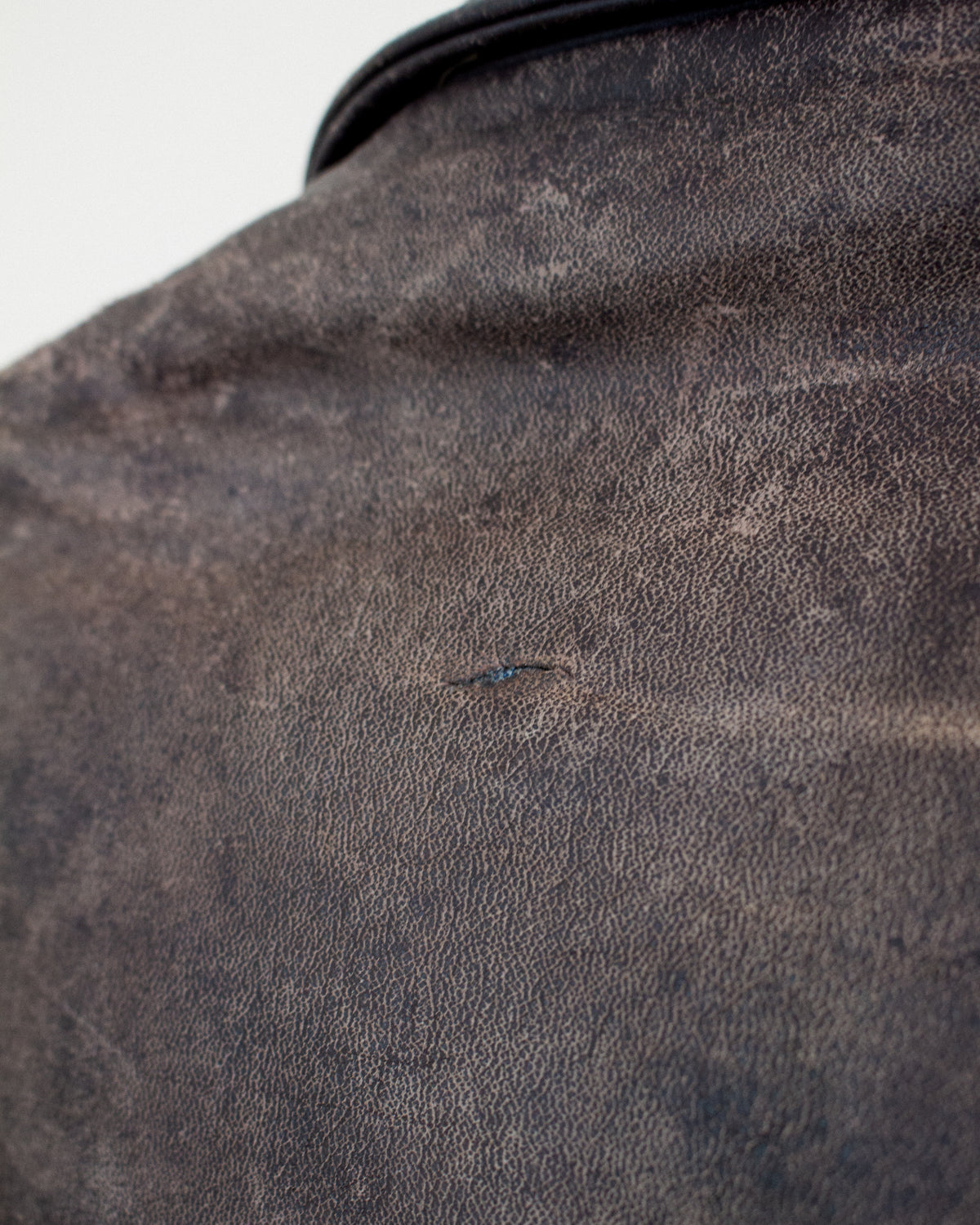 A close-up shot of a dark brown textured leather, showing a tiny hole on the surface.