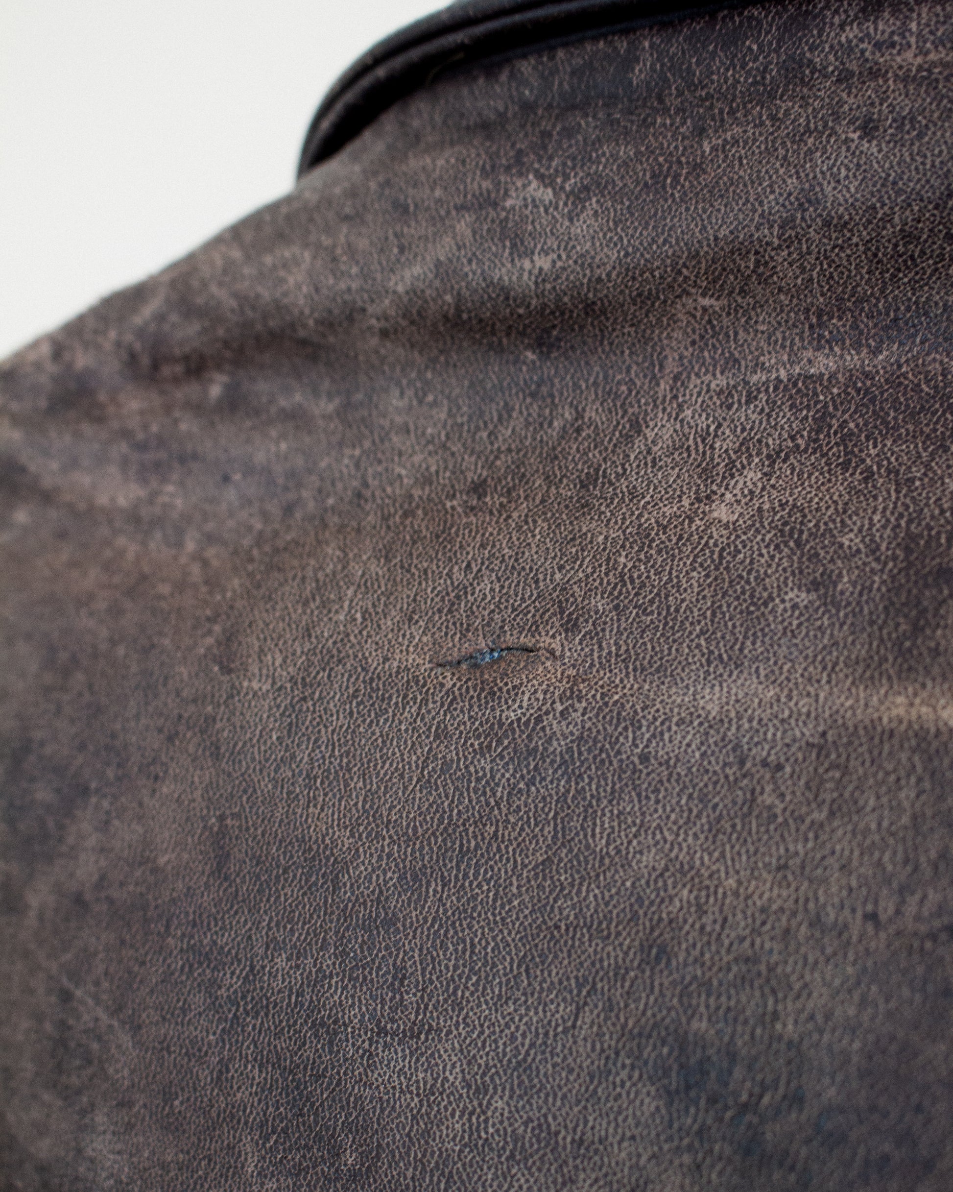 A close-up shot of a dark brown textured leather, showing a tiny hole on the surface.