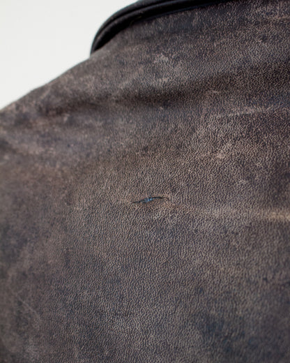 A close-up shot of a dark brown textured leather, showing a tiny hole on the surface.