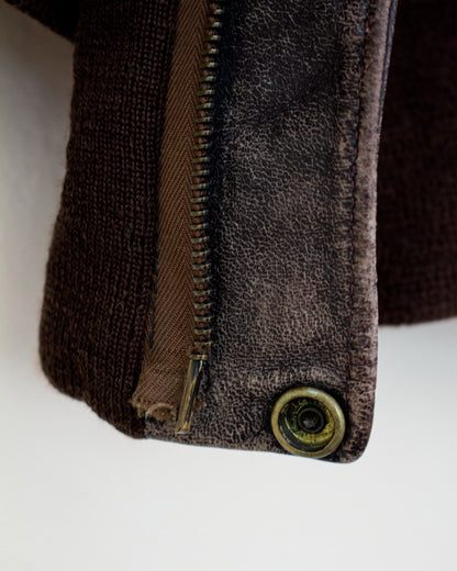 Close-up detail of a dark brown textured jacket showing a zipper, a brass snap button, and the fabric texture against a white background.
