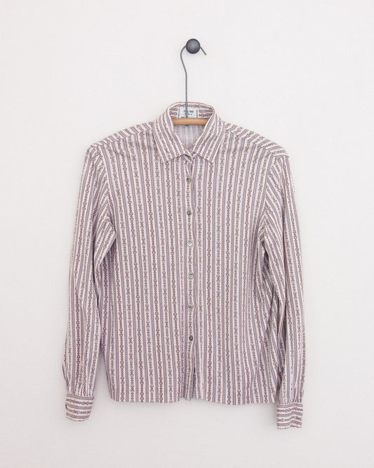 A long-sleeve button-up shirt with horse bit print in vertical stripes in muted pink, beige, white, and brown tones, hanging on a wooden hanger against a plain white wall.