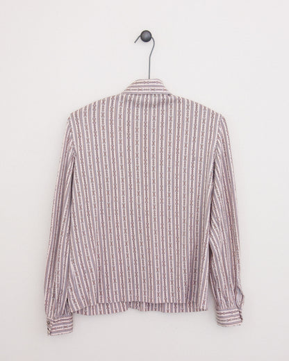 A long-sleeve button-up shirt with horse bit pattern in vertical stripes in dusty pink and brown and white, hanging on a black metal hanger against a plain white wall.