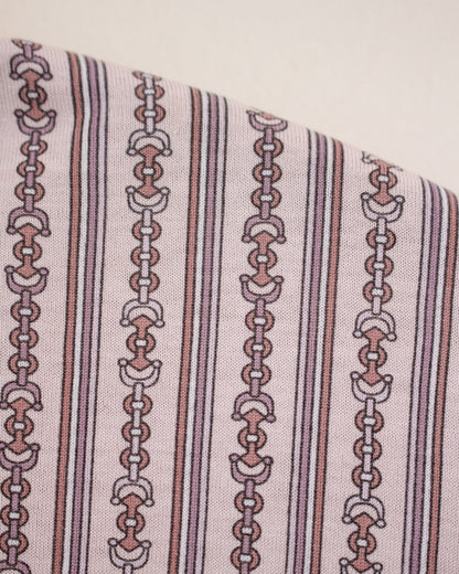 A close-up of a patterned fabric featuring vertical stripes and repeating horse bit chain motifs in muted pink, brown, and white on a light beige background.