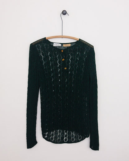 A dark green open-knit long-sleeve sweater with three brown buttons, hanging on a wooden hanger against a plain white wall.