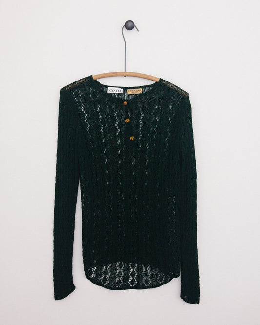 A dark green open-knit long-sleeve sweater with three brown buttons, hanging on a wooden hanger against a plain white wall.
