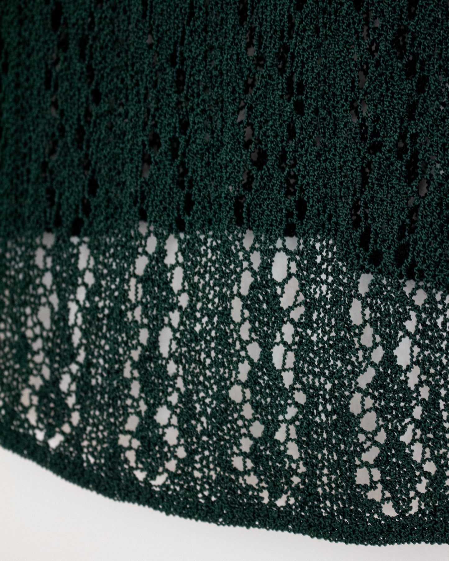 Close-up of a dark forest green lace fabric with a textured openwork pattern, draped over a white surface.