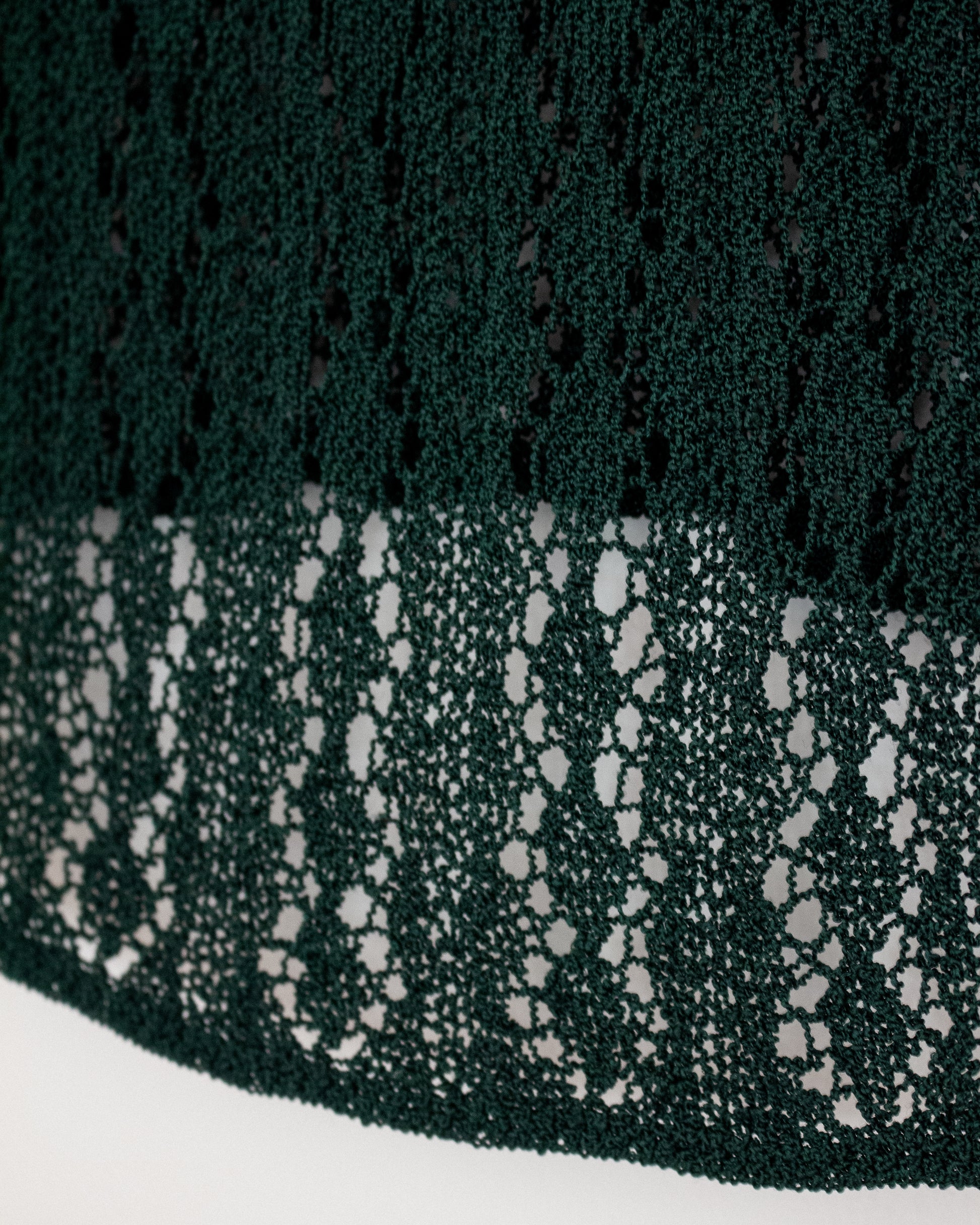 Close-up of a dark forest green lace fabric with a textured openwork pattern, draped over a white surface.