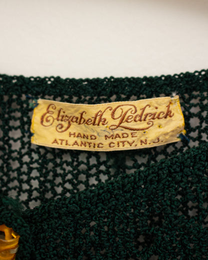 Close-up of a dark green crocheted lace textile with a vintage cream-colored brand label reading 'Elizabeth Ledrick' and 'Hand Made Atlantic City, N.J.