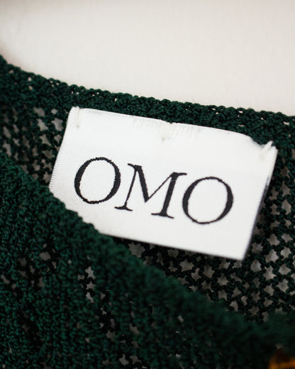 Close-up of a dark green lace garment with a white fabric label printed with the brand name 'OMO'.