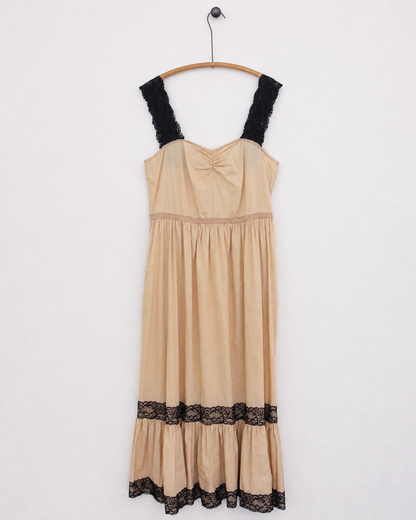 A beige slip dress with black lace trim on the straps and hem, hanging on a wooden hanger against a plain white wall.