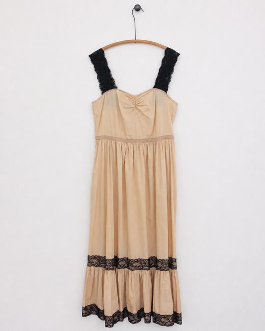 A beige slip dress with black lace trim on the straps and hem, hanging on a wooden hanger against a plain white wall.