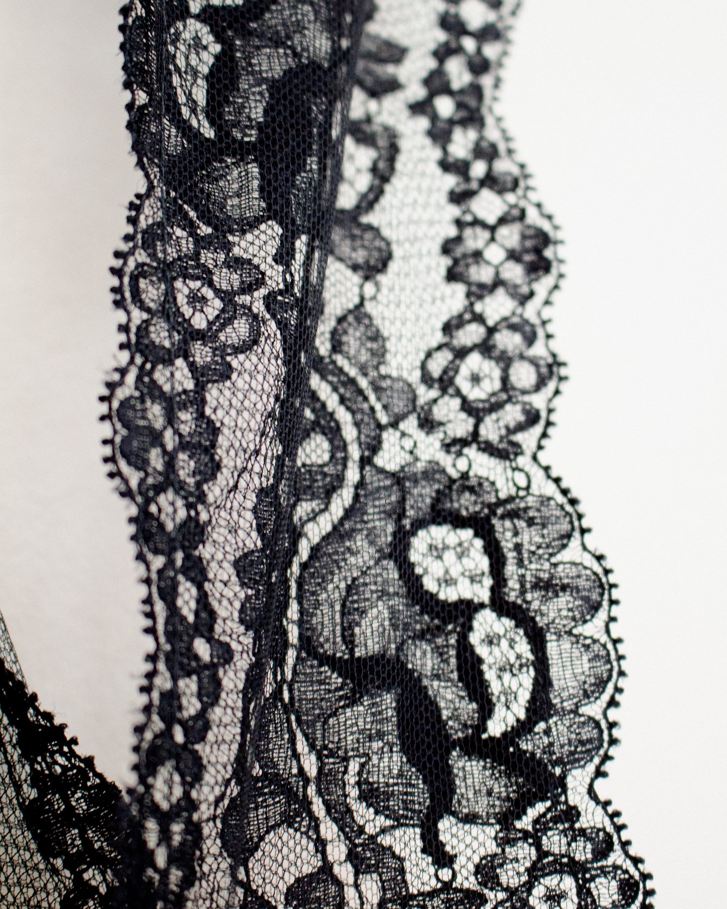 Close-up of a black floral lace trim with detailed mesh and scalloped edges against a plain white background.