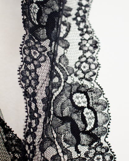 Close-up of a black floral lace trim with detailed mesh and scalloped edges against a plain white background.
