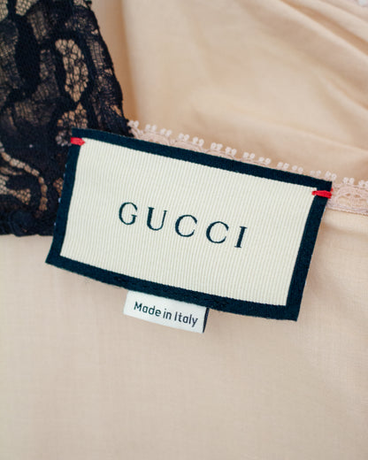Close-up of a Gucci garment label sewn onto light beige fabric with black lace trim, plus a small 'Made in Italy' tag below it.