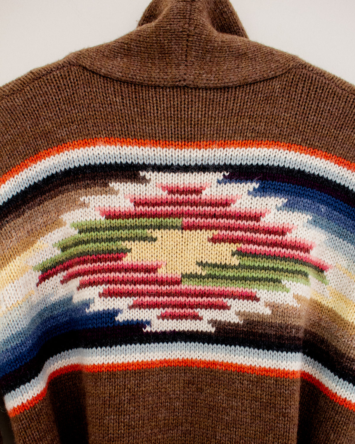 Close-up of a brown knit sweater featuring a Southwestern geometric pattern with red, green, blue, white, and orange stripes.