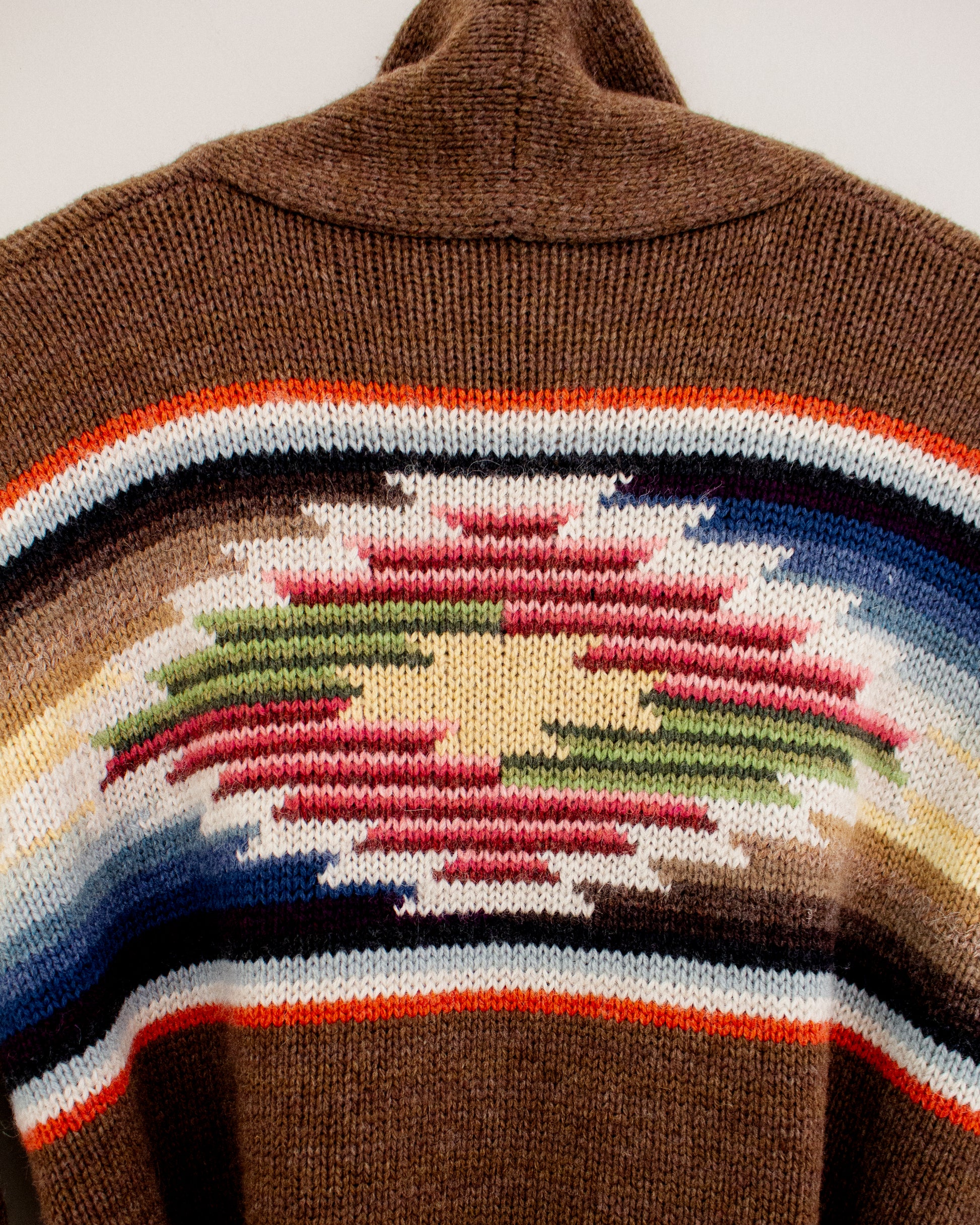 Close-up of a brown knit sweater featuring a Southwestern geometric pattern with red, green, blue, white, and orange stripes.