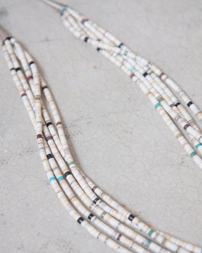 Close up view of vintage 5-Strand Santo Domingo Heishi necklace laying on white surface.