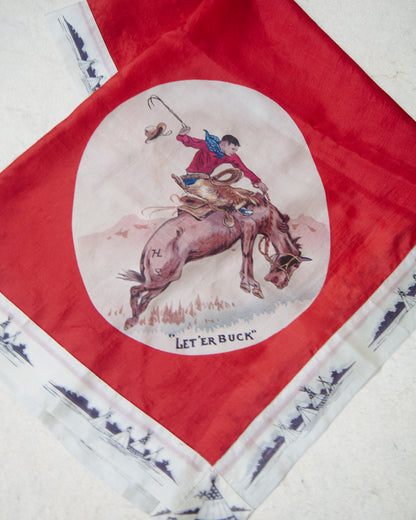 A square red scarf laid flat on a light textured surface, featuring a large circular western illustration of a rider on a bucking horse in the center and a white border with dark blue decorative print and the words "LET'ER BUCK" near the bottom.